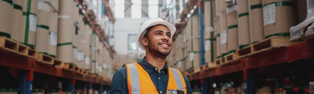 Portrait of young man wearing safety jacket holding digital tablet standing in factory warehouse